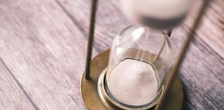 a clear glass hour glass with white sand on brown wooden table