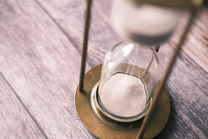 a clear glass hour glass with white sand on brown wooden table